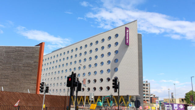 A tall white building with circular windows and yellow V-shaped supports with a Premier Inn sign