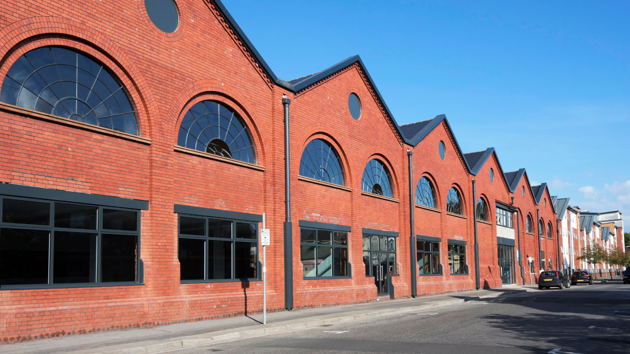 A long red brick building face shaped like several houses pushed together all along one side of a street