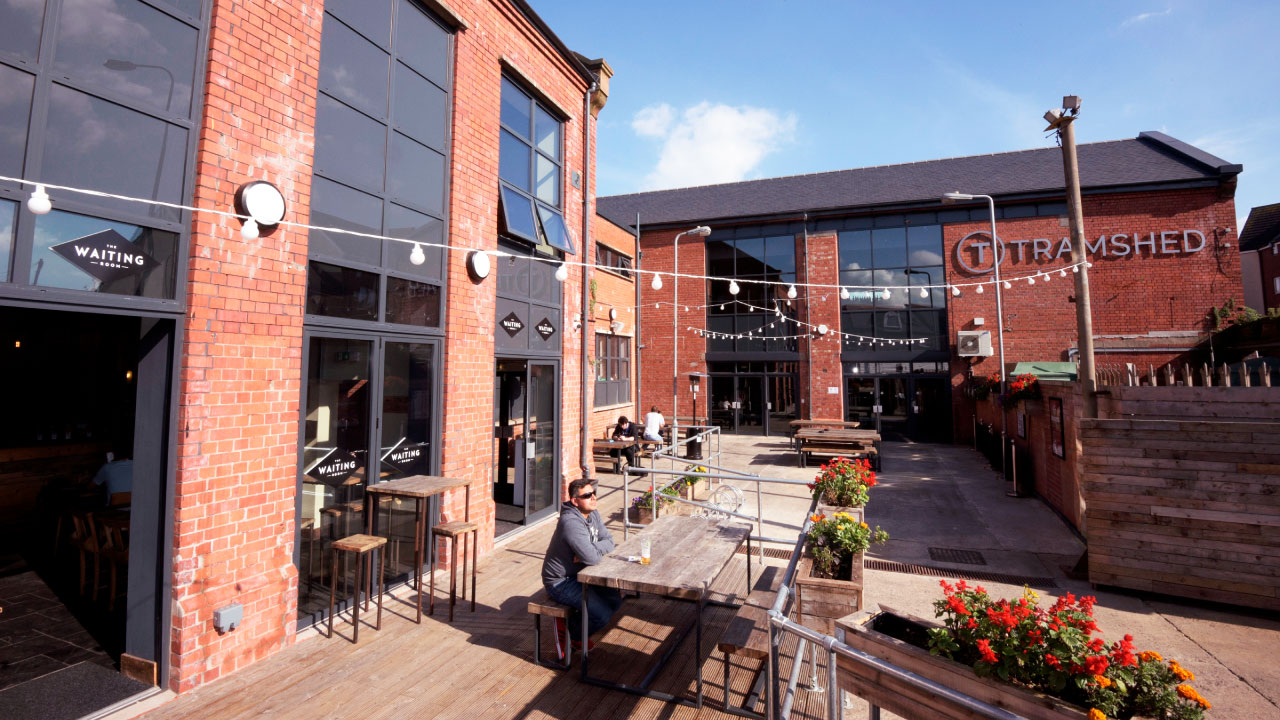 A person sitting at an outdoor cafe table under string lights outside the finished TramShed depot development