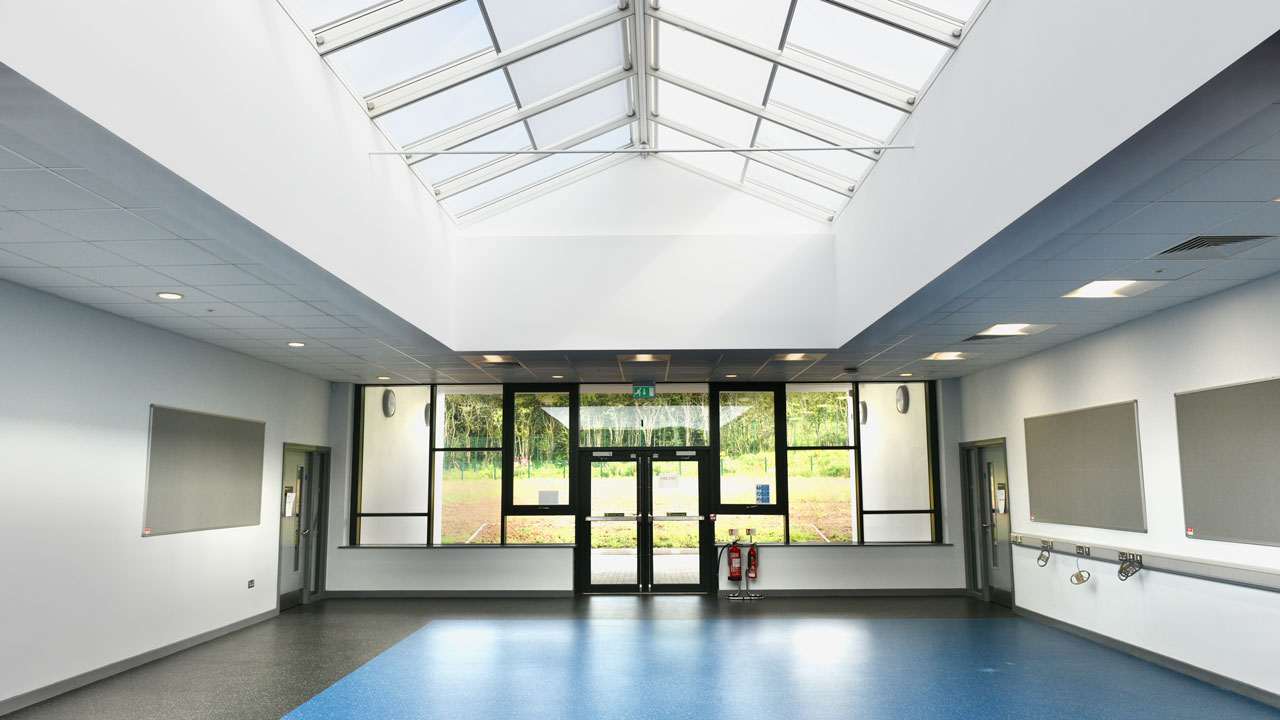 A wide hallway with natural light coming down from the skylight windows and ending in a wall with large windows and glass exit doors