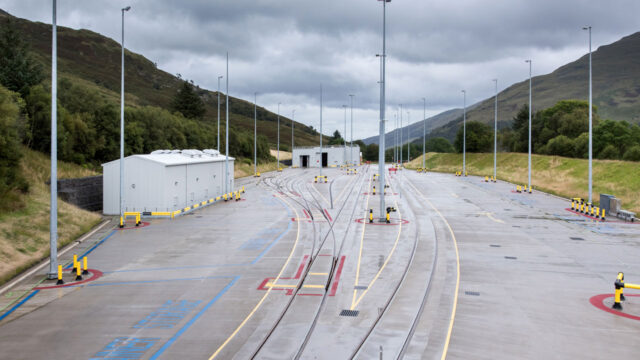 View of a road between mountains with rail tracks leading to a transfer point facility