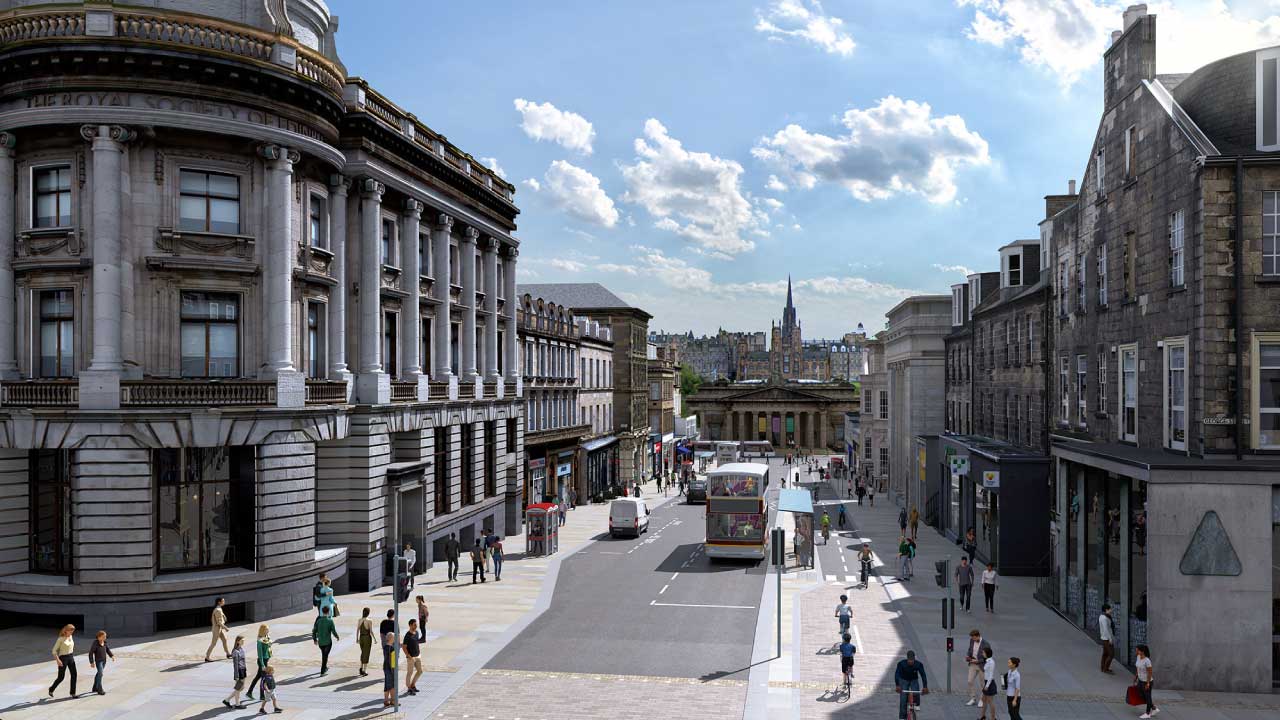 Downhill on street with wide pedestrian walkways beside buildings, traffic passing, blue skies overhead