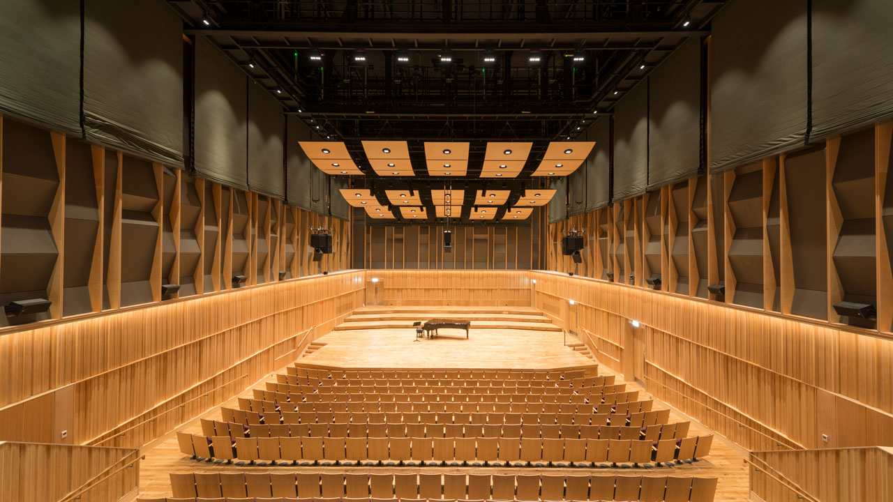 Empty conservatoire with rows of wooden seating facing a stage with a piano