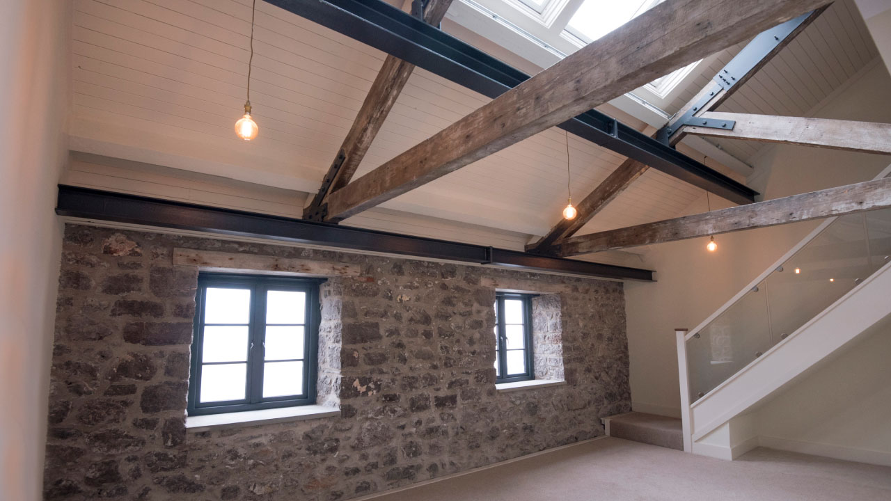 Interior room with exposed stone wall, wooden rafters, and staircase