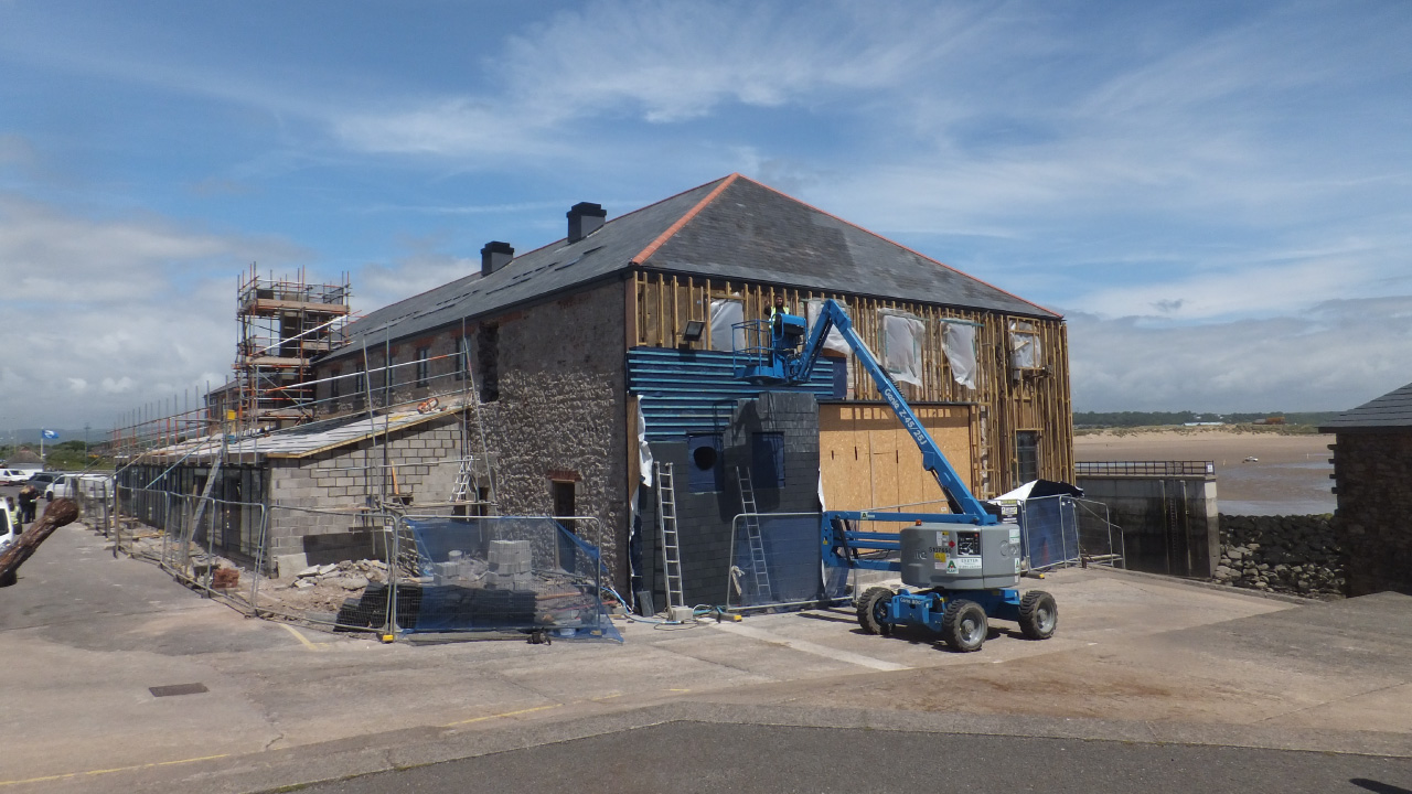 Large stone building under construction with scaffolding surrounded in fencing