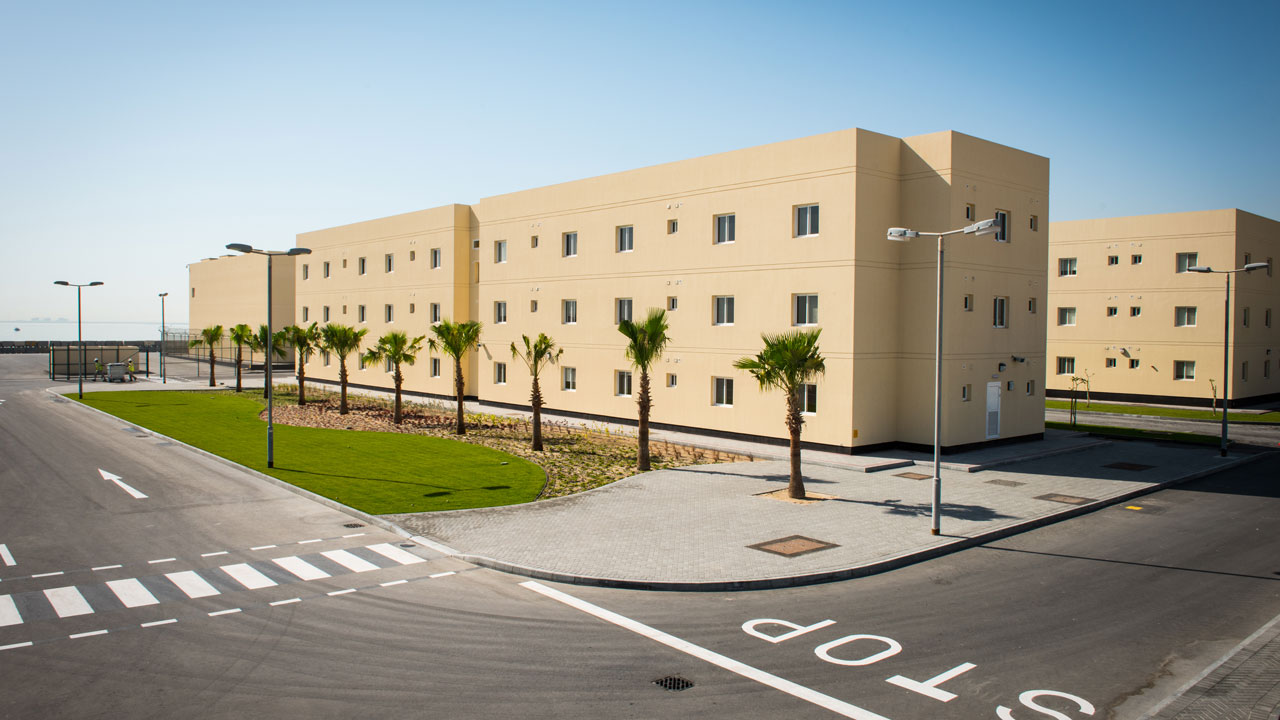 Beige three-story facility with inset windows, palms aligned in green space adjacent to the building