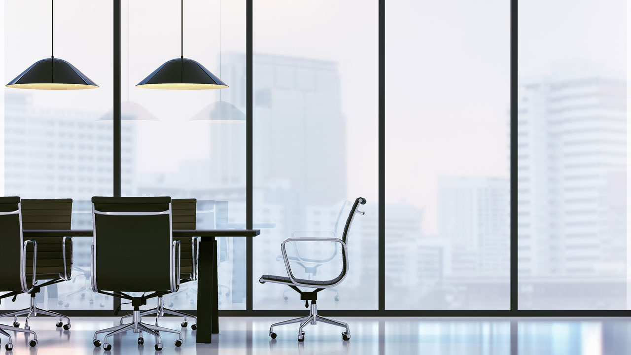 a smart office desk with chairs and overhead lamps in an office overlooking business buildings