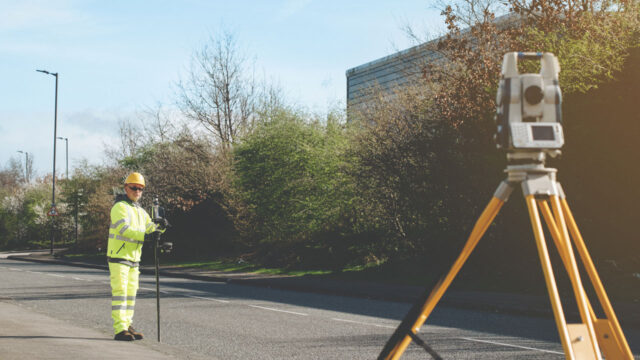 A man on a road in hi-visibility clothing conducting a geospatial survey