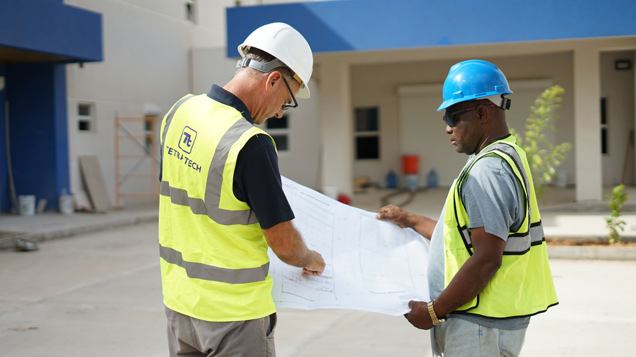 Two Tetra Tech employees wearing hi-vis vests looking at a project plan sheet