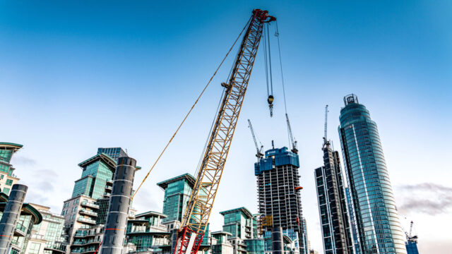 High-rise buildings and construction cranes in front of a blue skyline