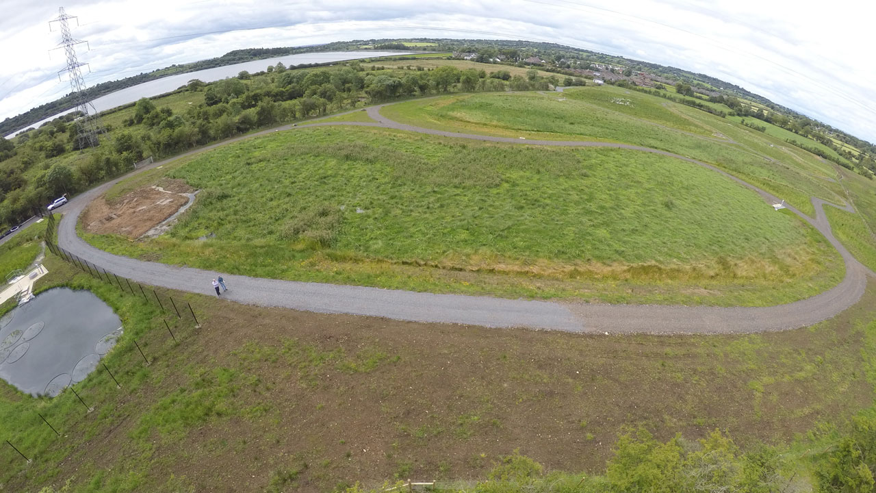 Closer view of the same rural field, two distant people standing on the road by the pond