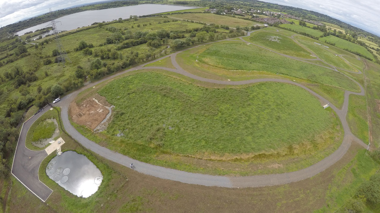 Different angle of a rural field with a small pond and bean-shaped road, a larger lake in the background