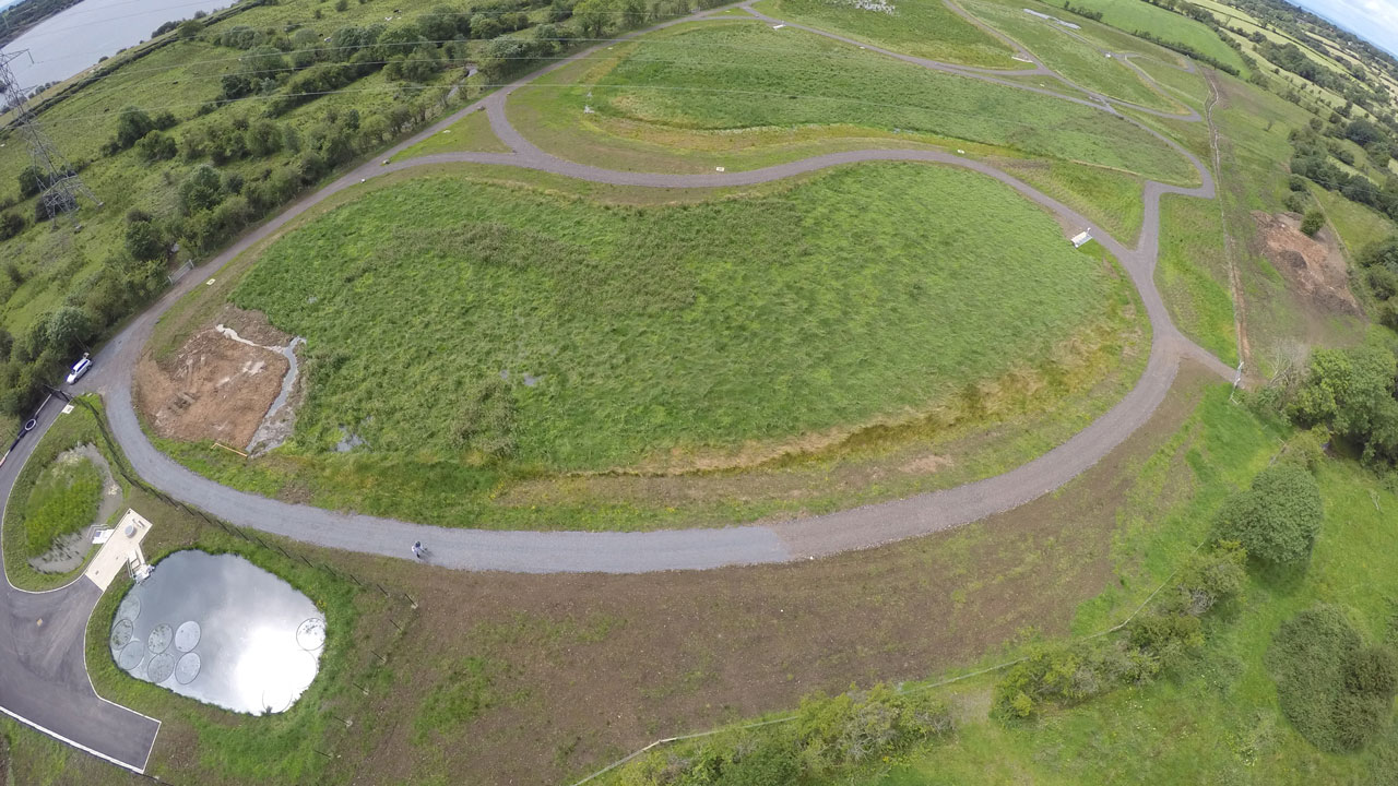 Aerial view of a rural field with a small pond and bean-shaped road running by it