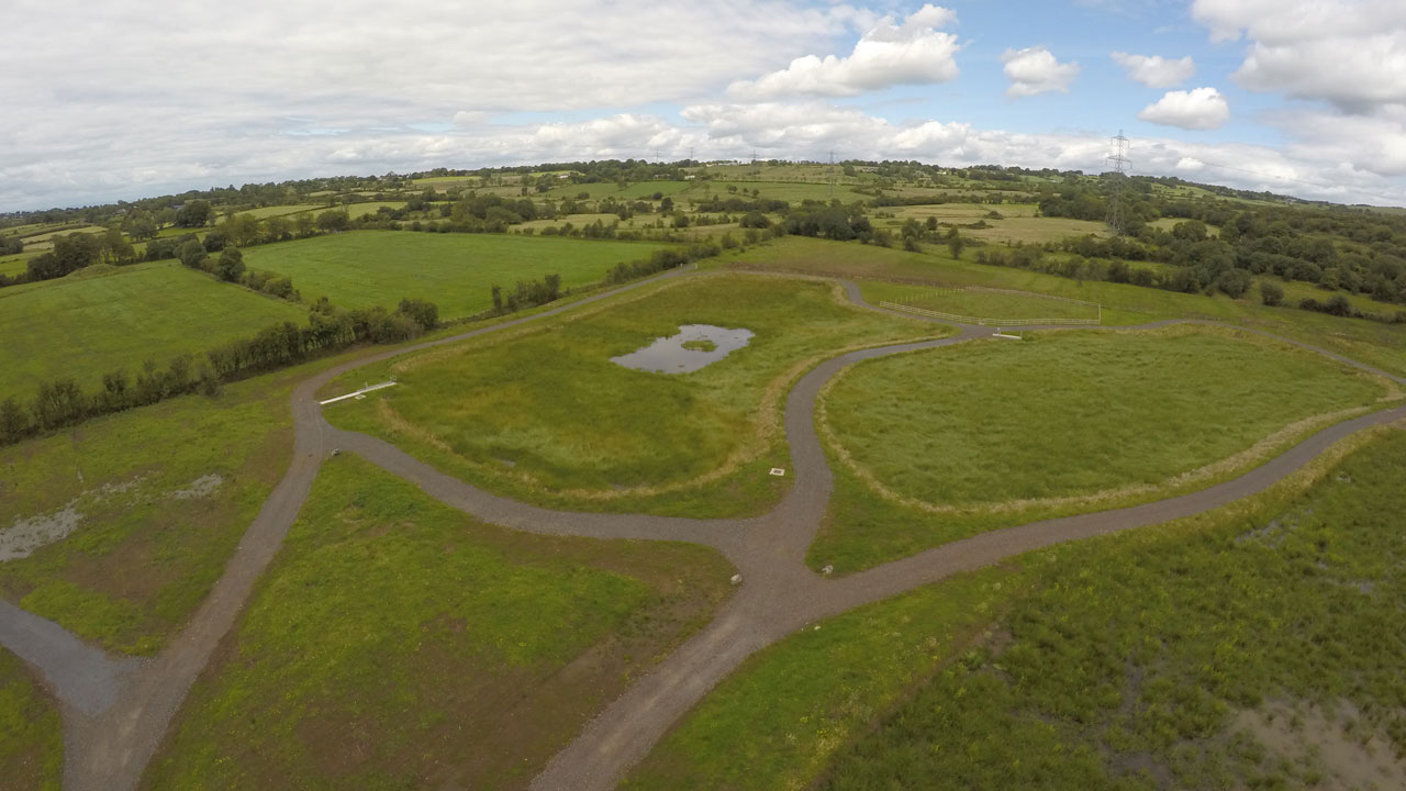 A rural field with a small pond and dirt paths winding through it