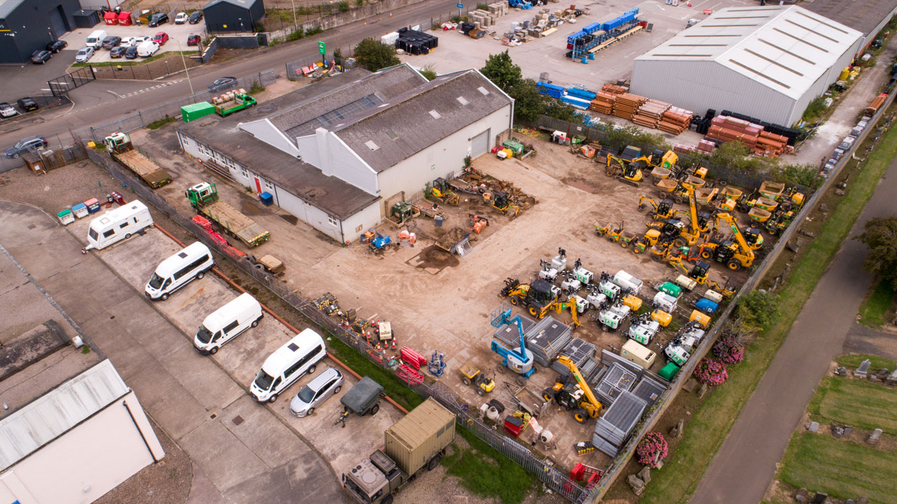 Angled aerial view of the warehouse and vehicle-filled parking lot of a construction company