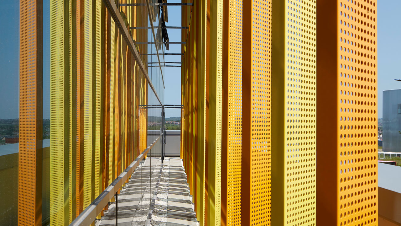 Closer view of orange and yellow metal panels with circular grates on the building balcony patio