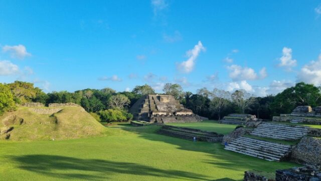 An image of a green field and stone buildings below a blue sky in belize