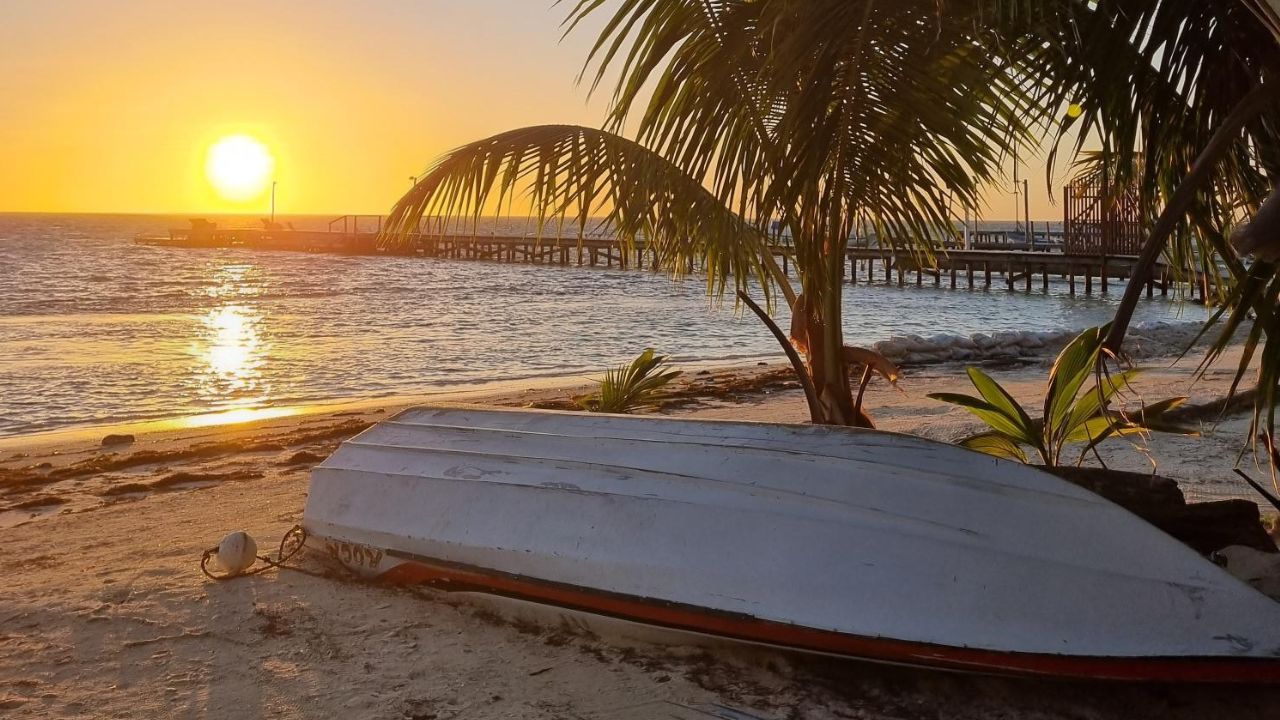 An upturned small white boat resting on a beach in belize by the ocean looking out on a sunset